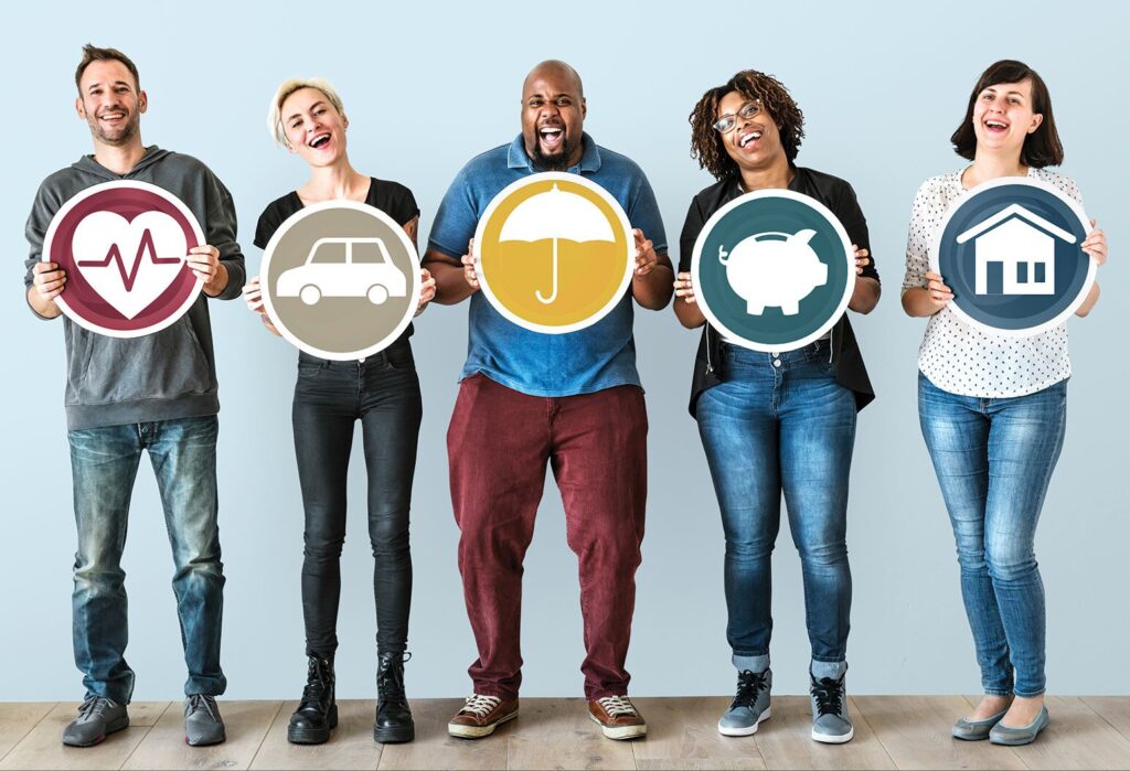 Five people standing in a row, each holding a circular icon representing health, car, umbrella (insurance), savings (piggy bank), and home, smiling and facing the camera against a light background.