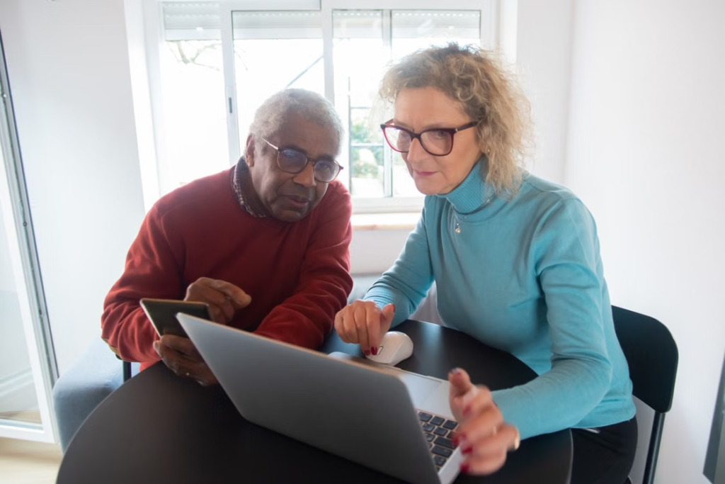 An older man and woman sitting at a table using laptop computers at home