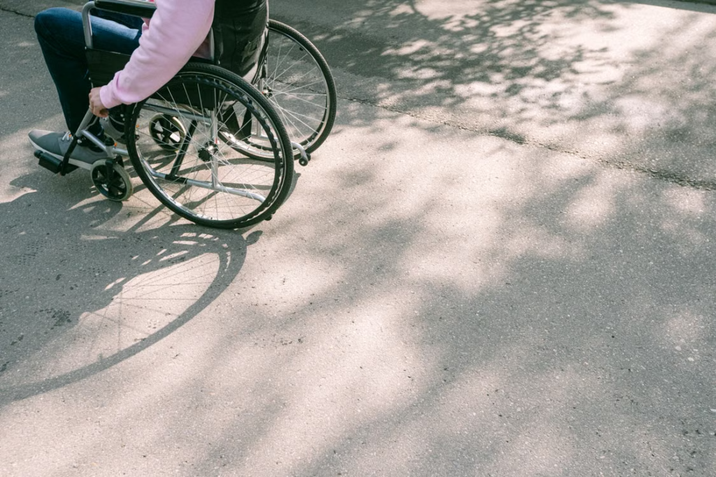 A person in a wheelchair moving along a sunlit road with tree shadows